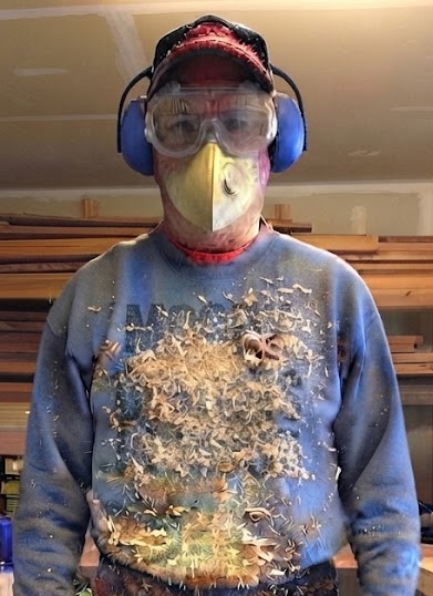 Jim in safety goggles, ear protection and a dust mask, covered in wood shavings